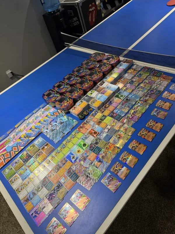 A full Pokémon collection laid out on a table — tins, sorted singles, and sealed product
